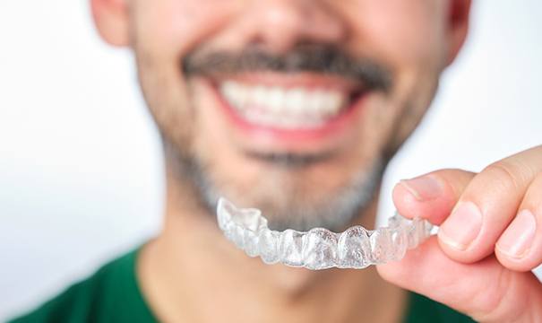 Man with facial hair holding clear aligner