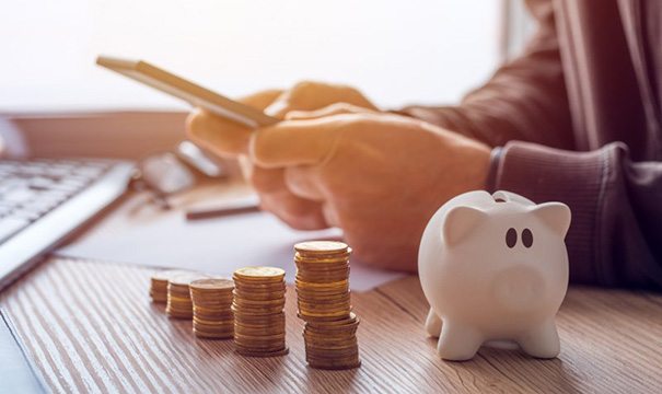 Individual using a calculator next to coin stacks and a piggy bank