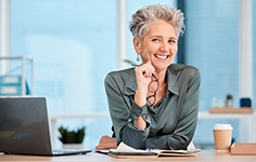 Woman with dental implants smiling at desk