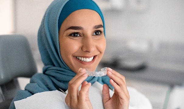 Woman smiling while holding clear aligner in treatment room