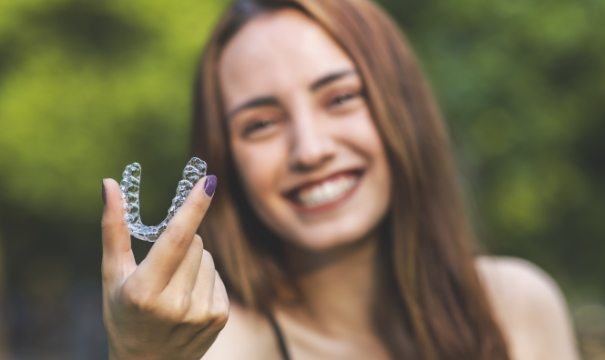 Smiling woman holding a ClearCorrect aligner