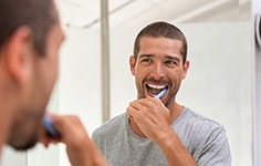 A man brushing his teeth while looking at the bathroom mirror