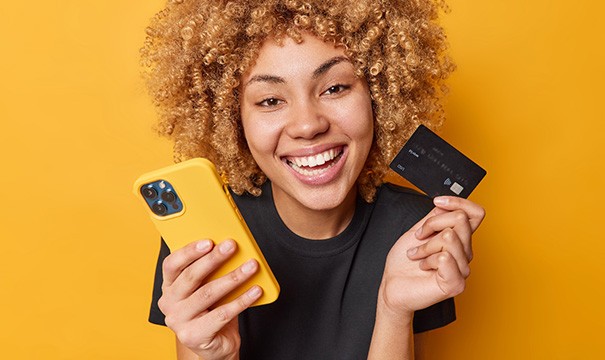 Smiling young woman holding her phone and a credit card