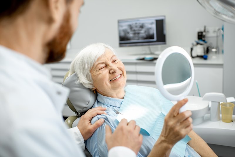 An older woman checking her smile in the dentist's mirror