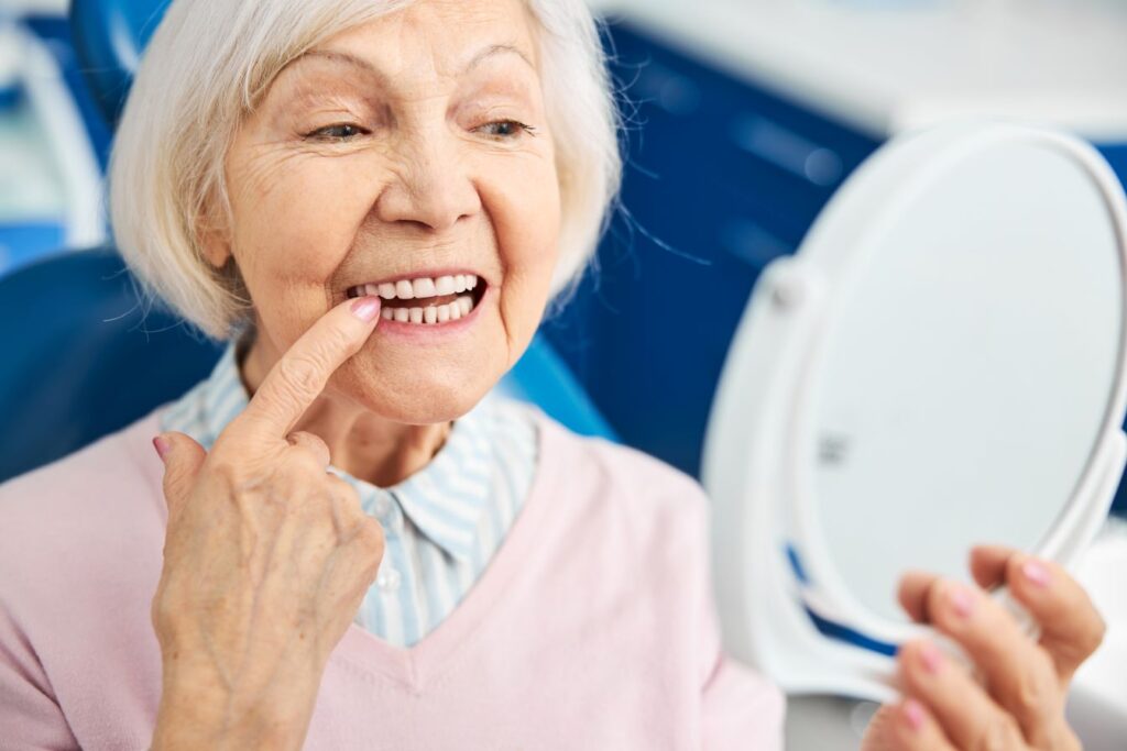 An older woman looking at her teeth in a mirror