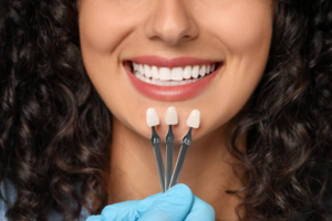 Woman smiling while dentist compares dental veneers to her teeth